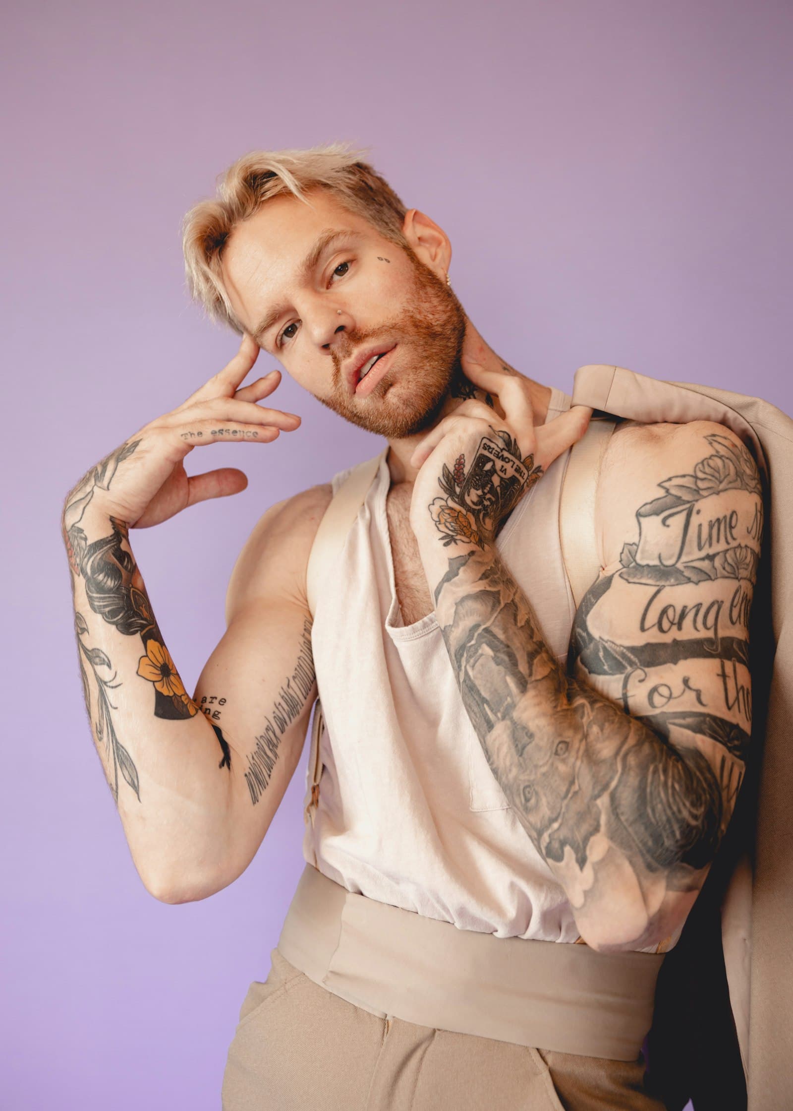 Tattooed man posing against a lavender studio backdrop